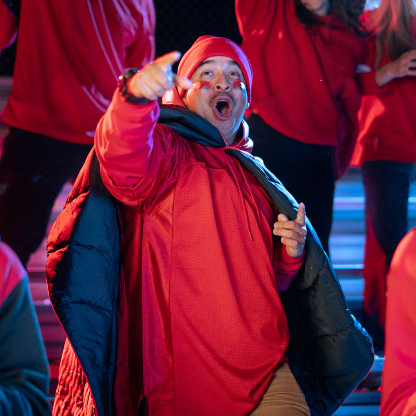 A person in a red outfit enthusiastically gestures in a crowd.