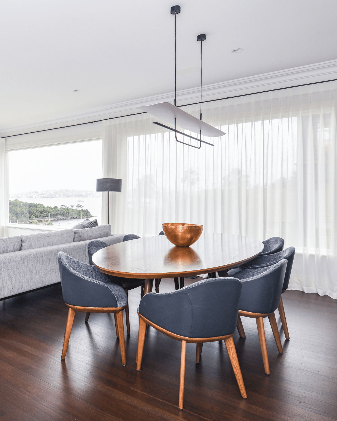 Reflector Linear Pendant hanging above an oval timber dining table in a bright modern interior