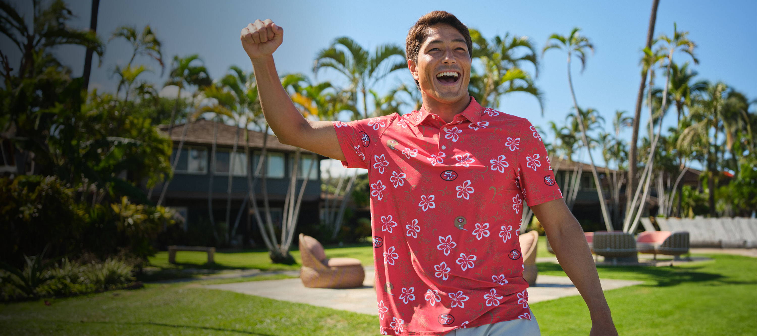 Person in a pink shirt joyfully celebrating in a tropical setting.