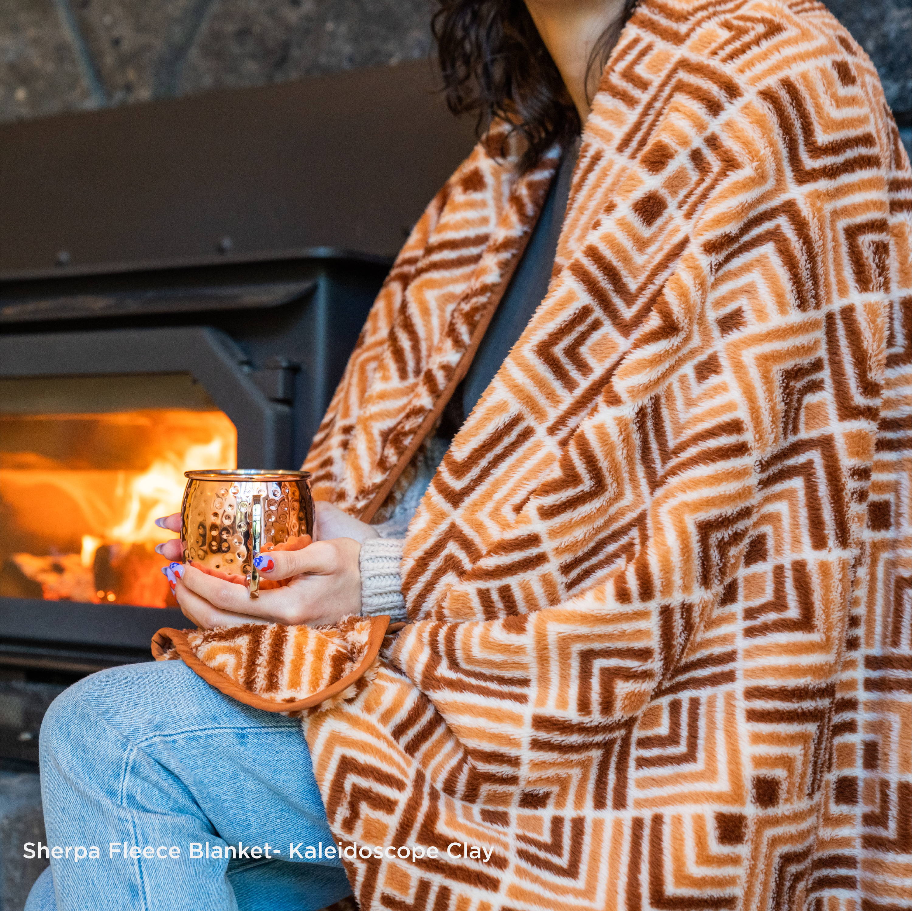 Person wearing Rumpl Sherpa Fleece blanket sitting by fire