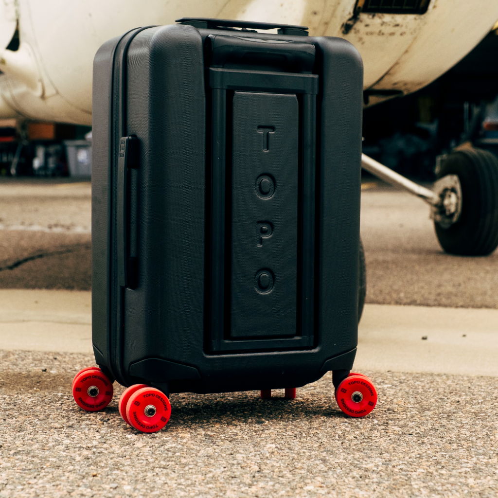 A black suitcase with red wheels positioned near an airplane.