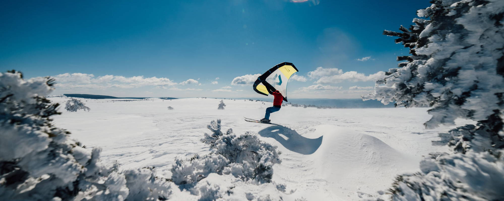 Un homme ride en wingsnow avec ses skis sur un plateau montagneux enneigée et vallonné .