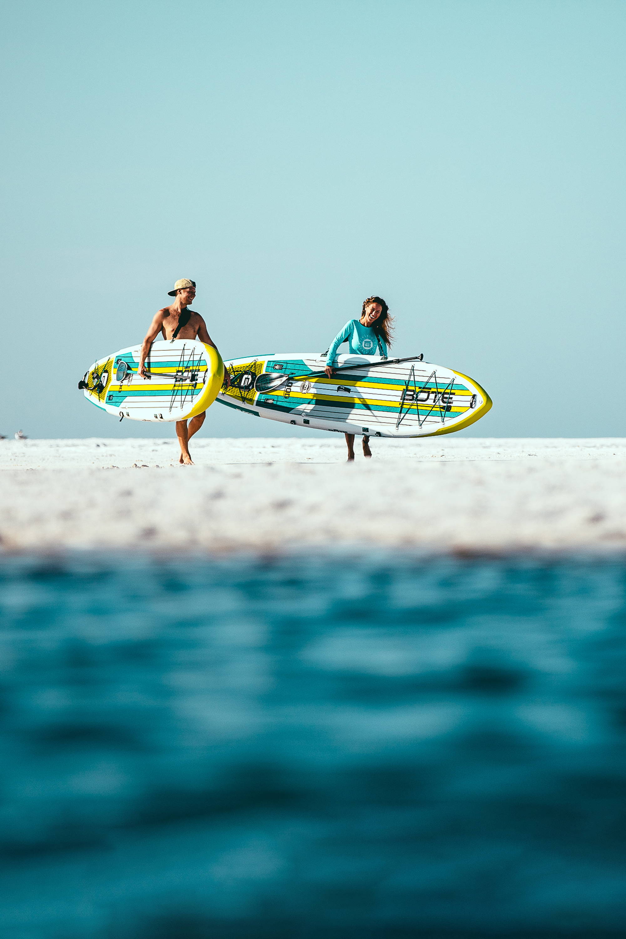Two people carrying BOTE Flood Aero Inflatable Paddle Boards