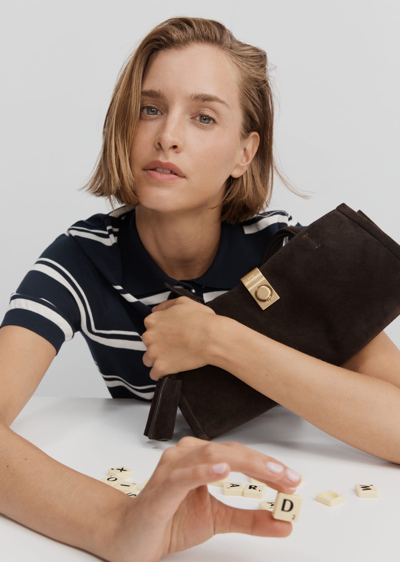 A woman in a striped shirt holding a clutch with letter tiles on the table.