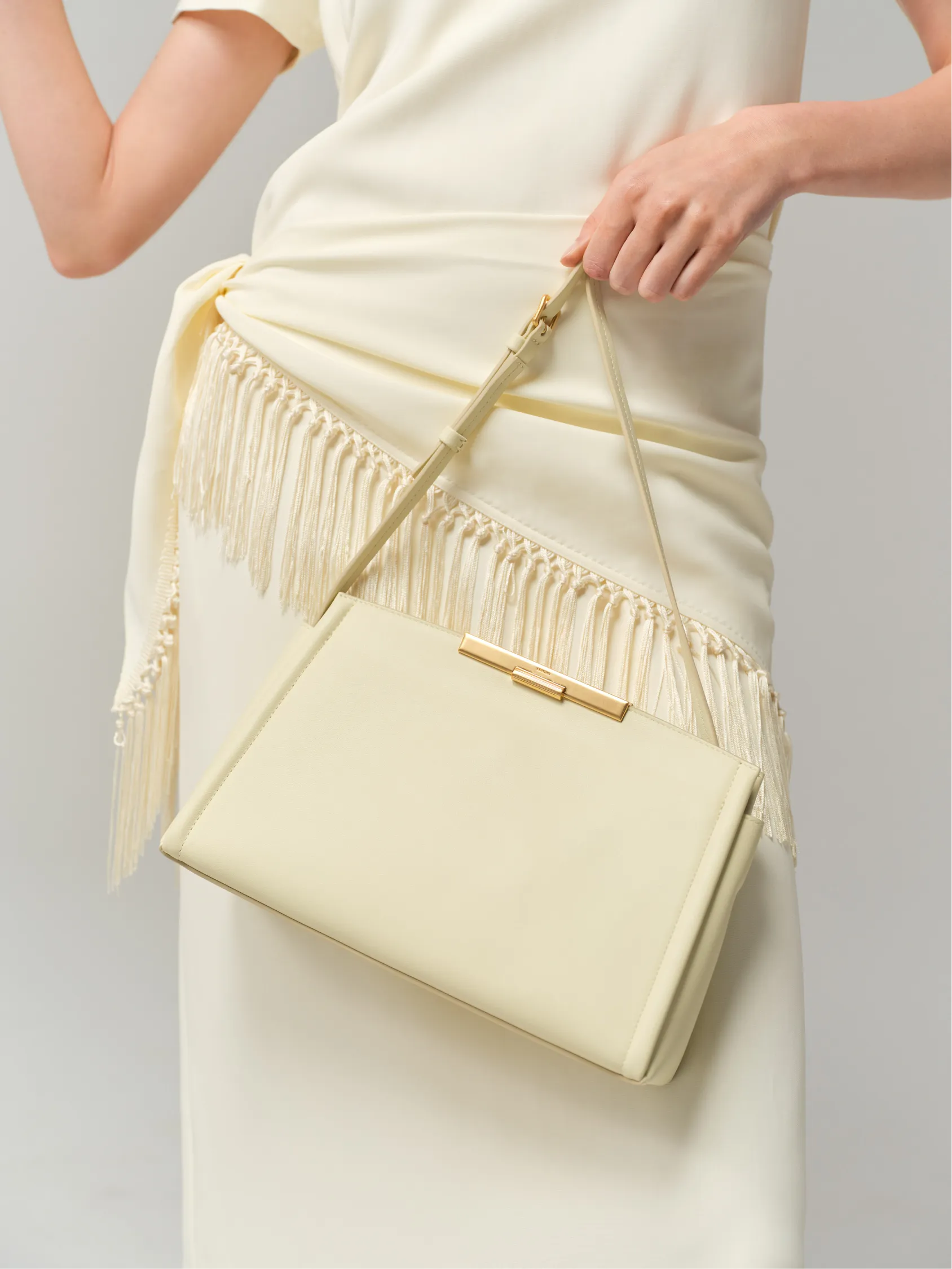 A person holding a cream-colored handbag with fringe details on a dress.