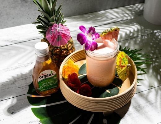 A tropical drink garnished with flowers, surrounded by fruits and a honey bottle.