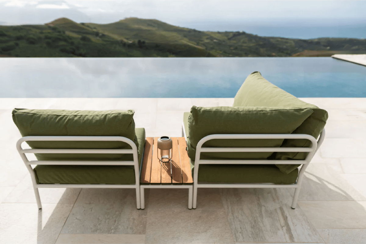 Outdoor lounge chairs with green cushions overlooking an infinity pool for a relaxed resort style backyard.