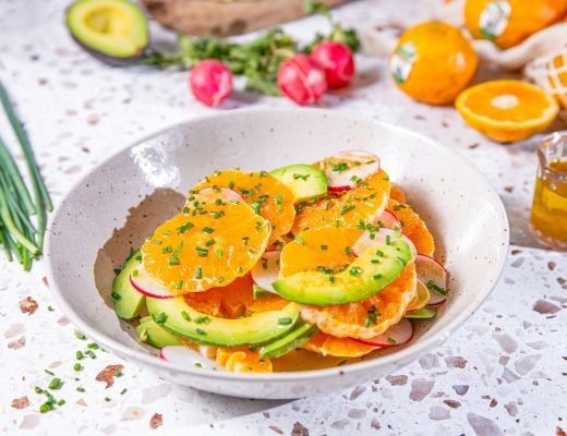 Colorful salad with oranges, cucumbers, radishes, and green herbs in a bowl.