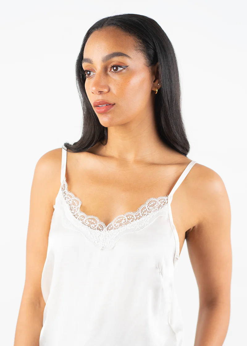 A model wearing an off white satin camisole with lace detailing around the neckline