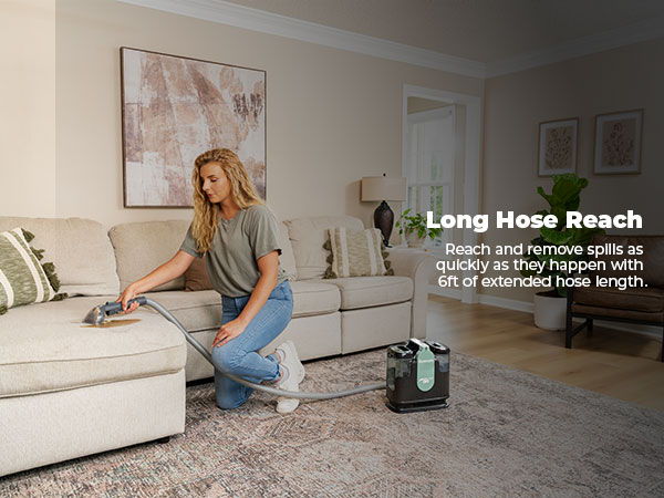 Person using a vacuum cleaner with a long hose near a couch.