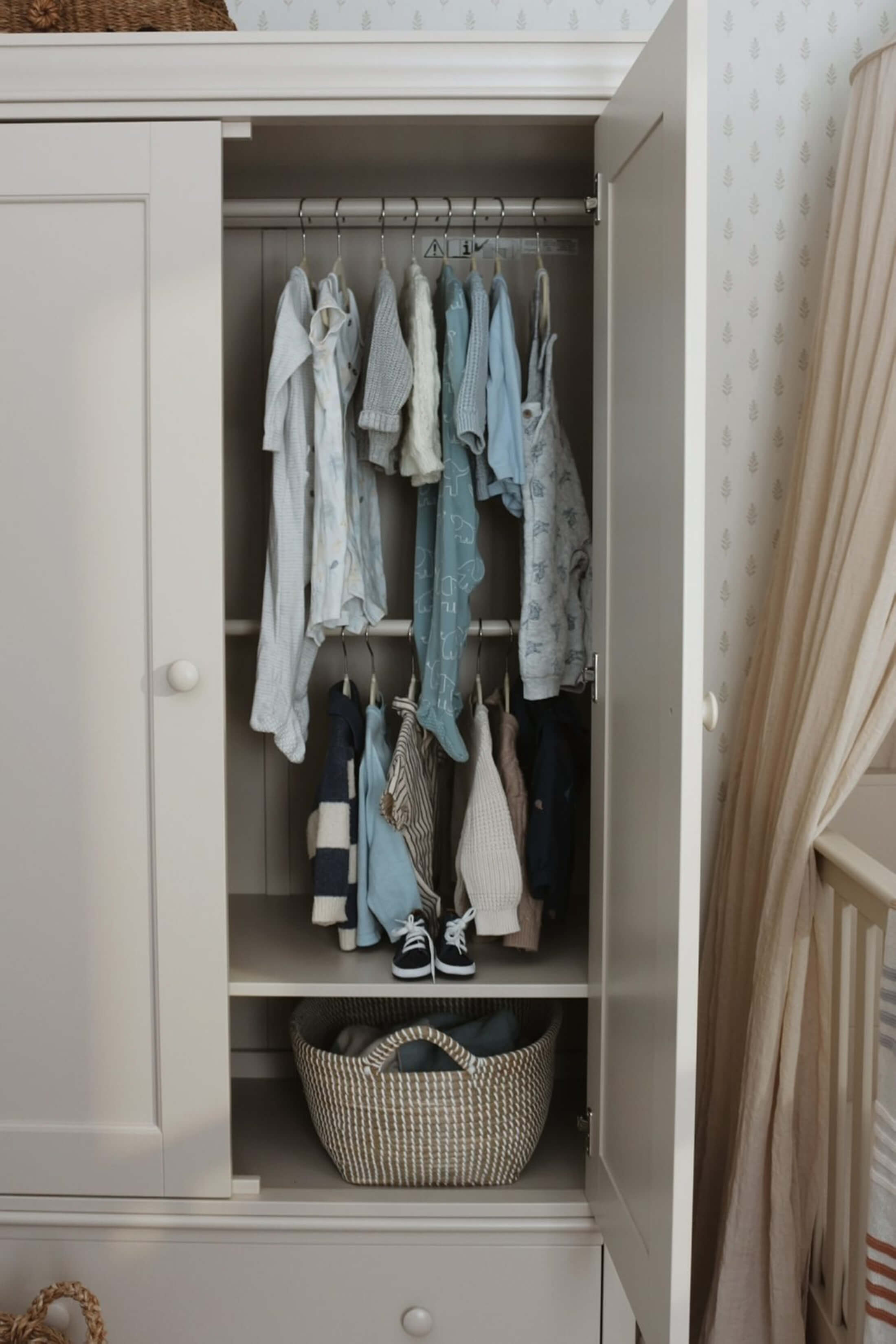 A closet with hanging clothes and a woven basket on a shelf.