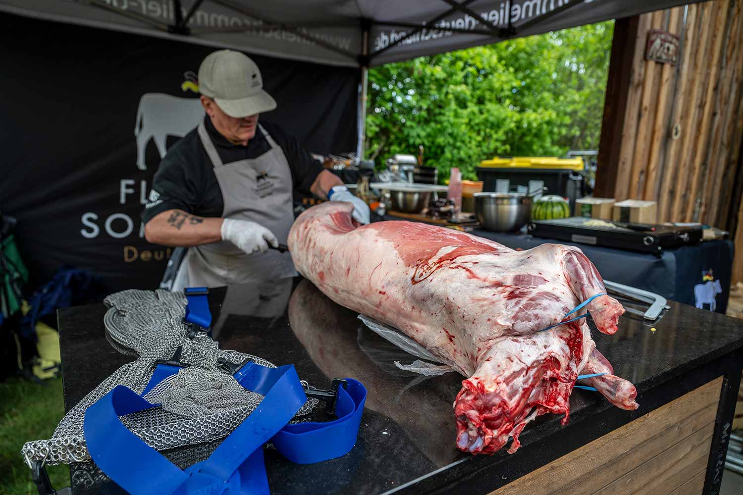 Person preparing meat on a table at an outdoor event.