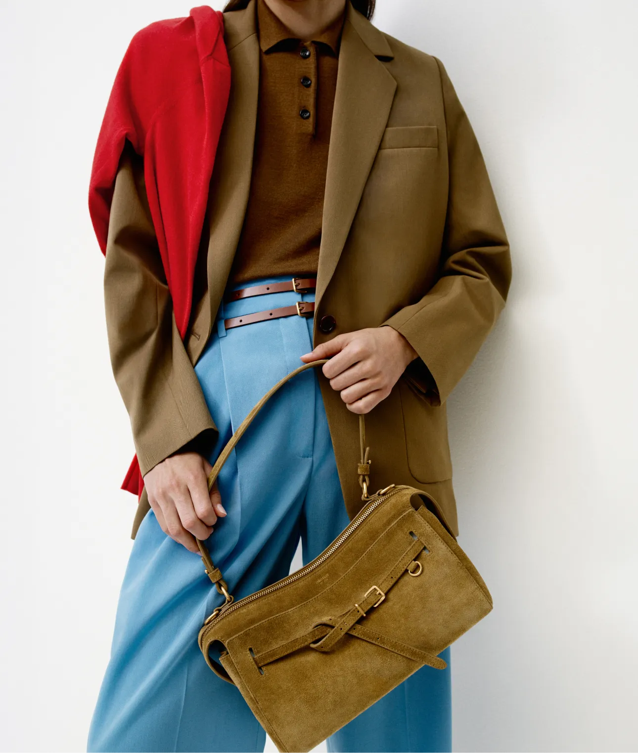 Person wearing a brown blazer, blue pants, and holding a brown bag.