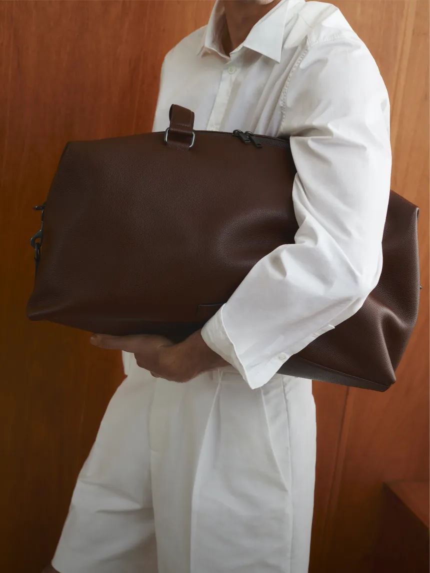 Person holding a large brown bag, wearing a white outfit.