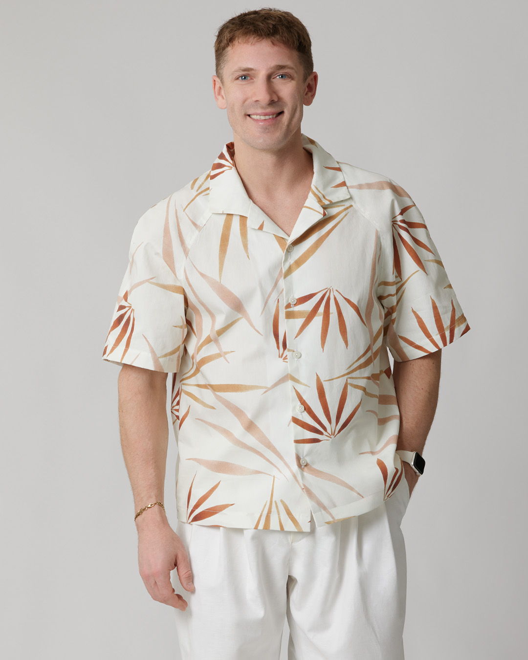 Smiling man in a patterned short-sleeve shirt and white pants.