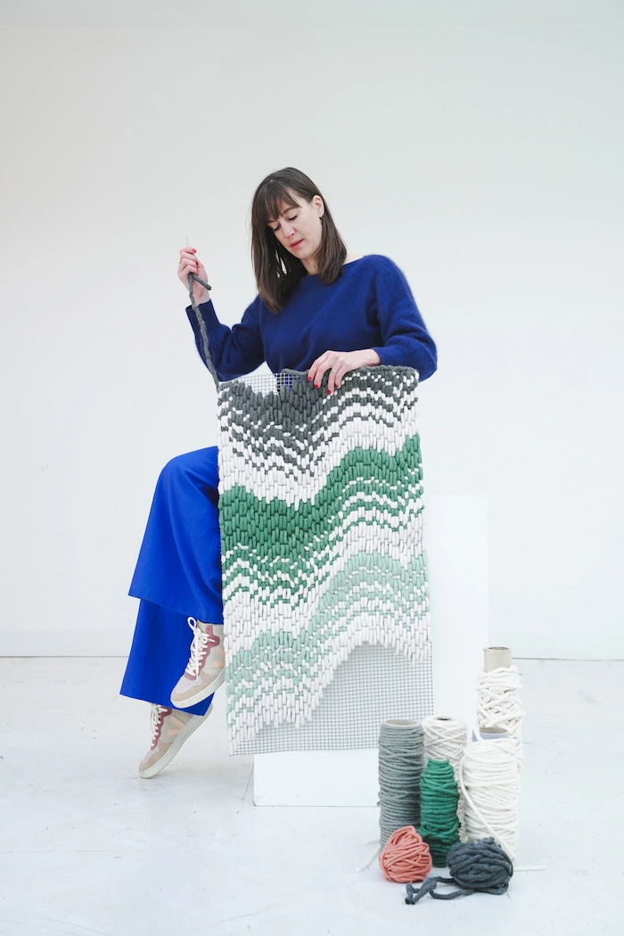 Designer Charlotte Lancelot knitting a patterned tapestry with yarn in various colors.