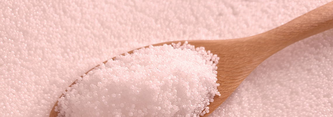 A wooden spoon filled with pink salt on a textured surface.