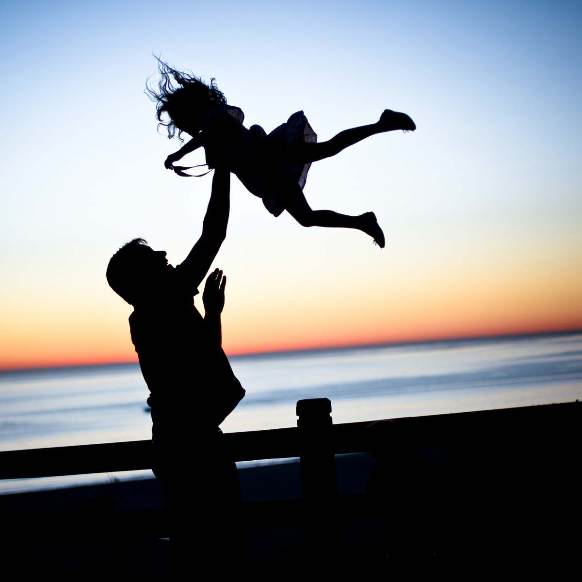 A father and child in silhouette. The child is being thrown in the air.