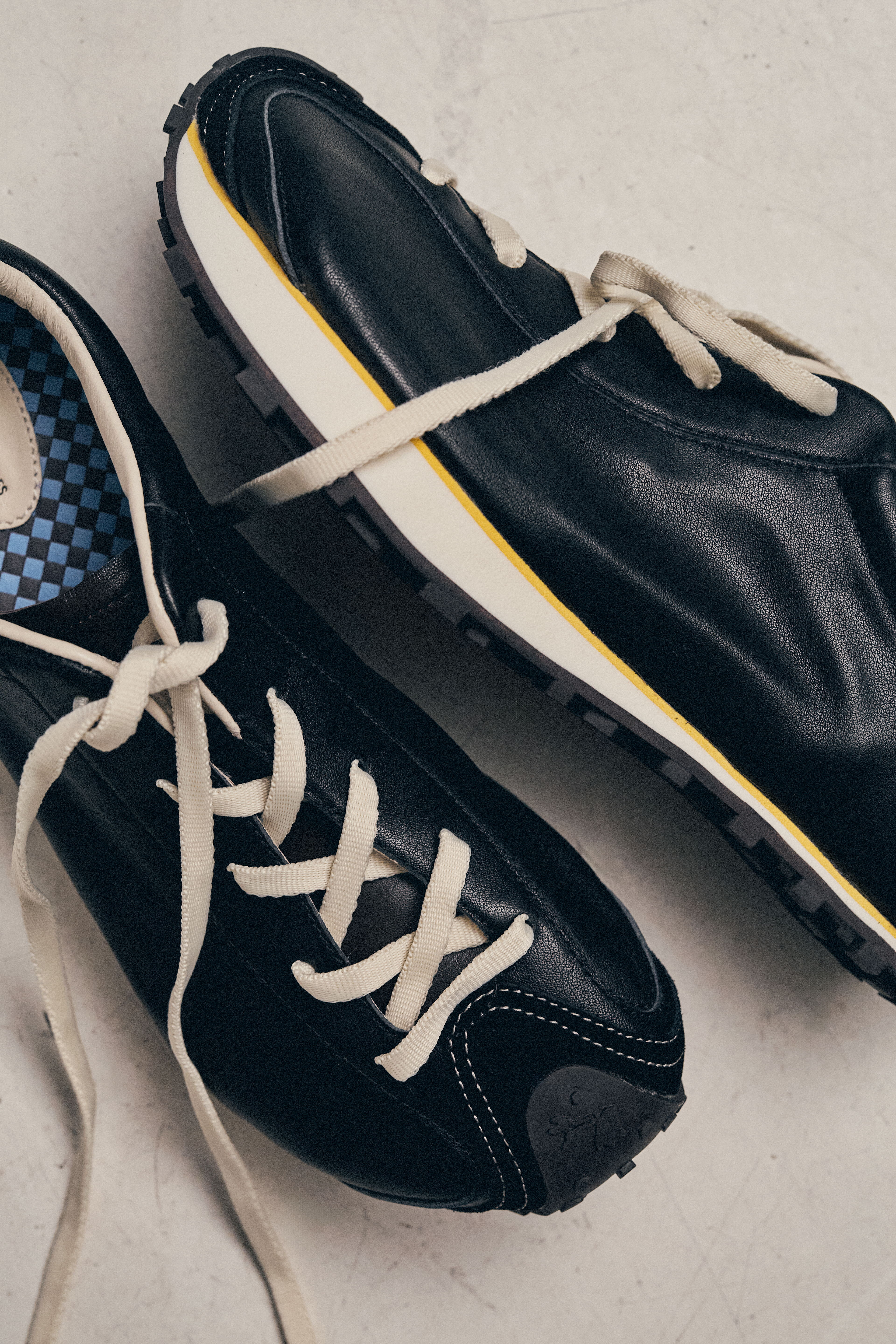 A pair of black sneakers with white laces on a light background.