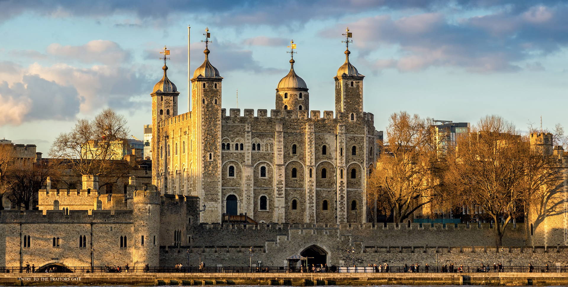 A picture of the Tower of London bathed in yellow sunlight taken from across the River Thames, White Tower standing clear in the centre. 