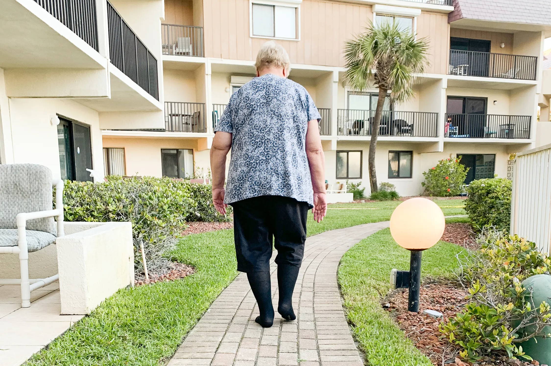 Elderly woman walking on sidewalk, wearing compression socks