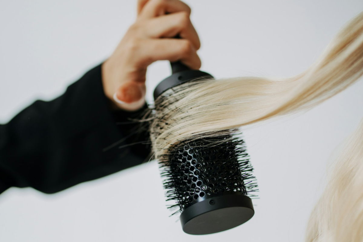 Hair Education Course Webpage Image - Hand holding a metal round brush, styling a strand of blonde hair