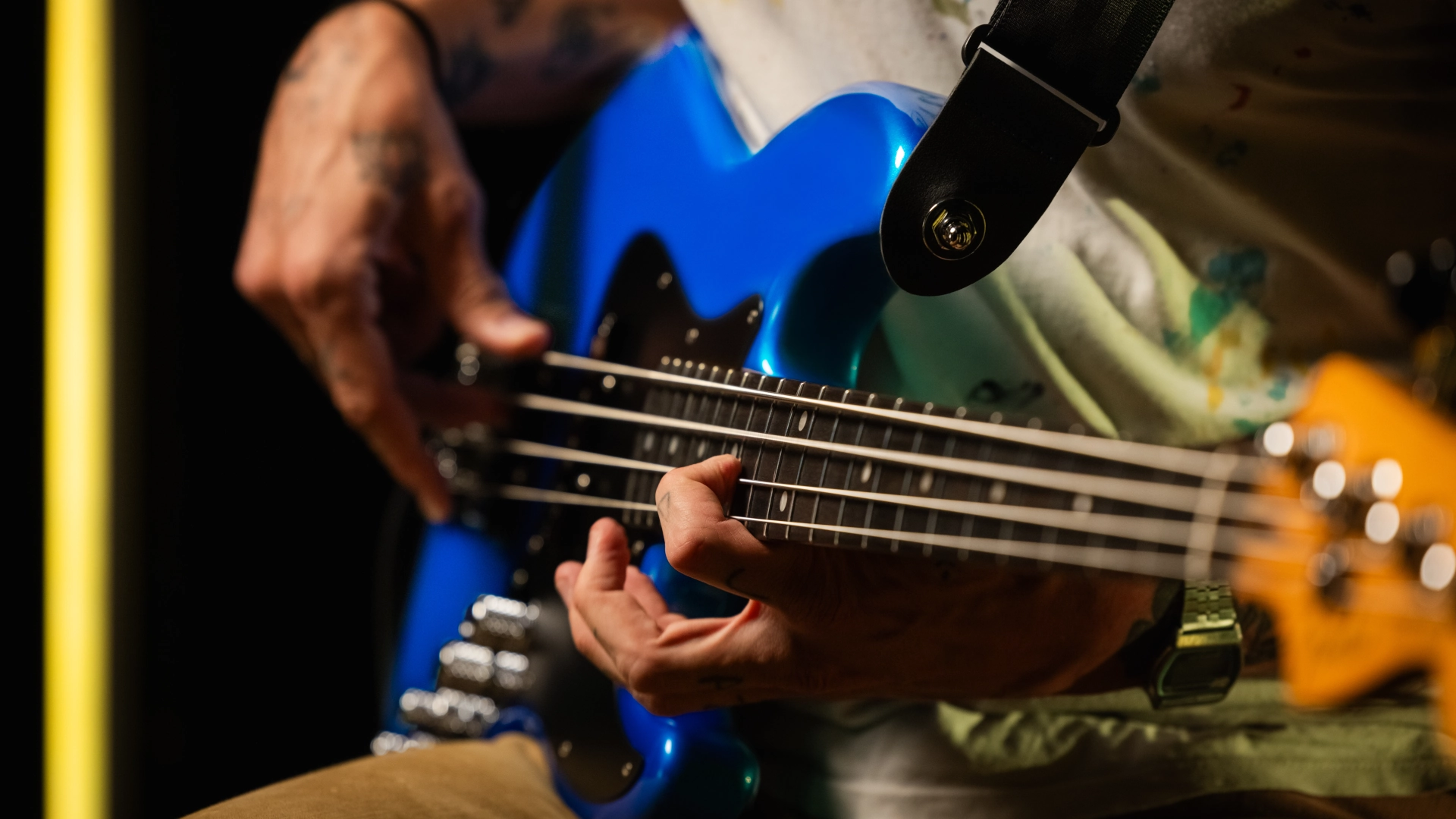 A close-up of hands playing a blue electric bass guitar.