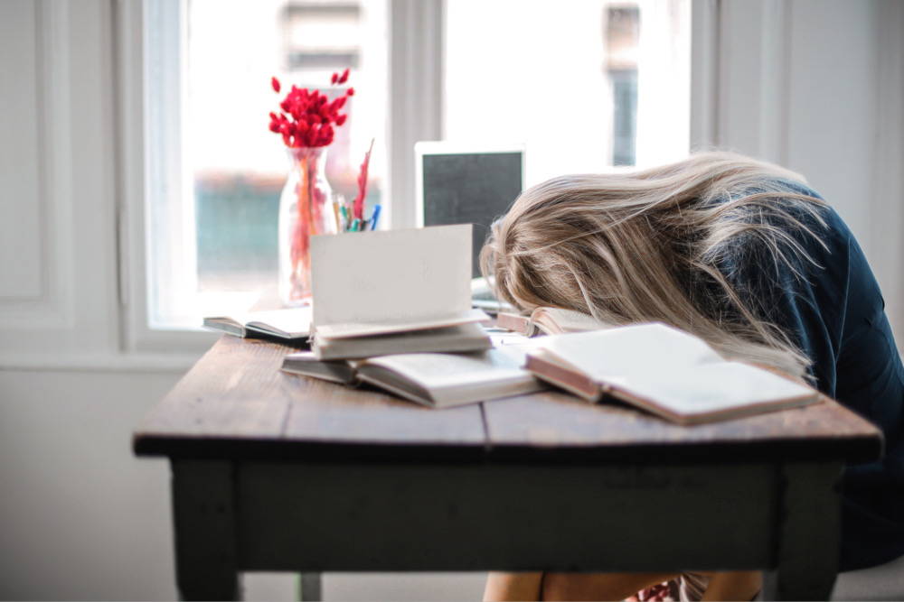 Tired woman resting her head on a table covered with books.