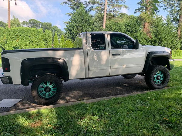 Side profile Caitlyn's lifted white Silverado with teal wheels and fender flares photo 2
