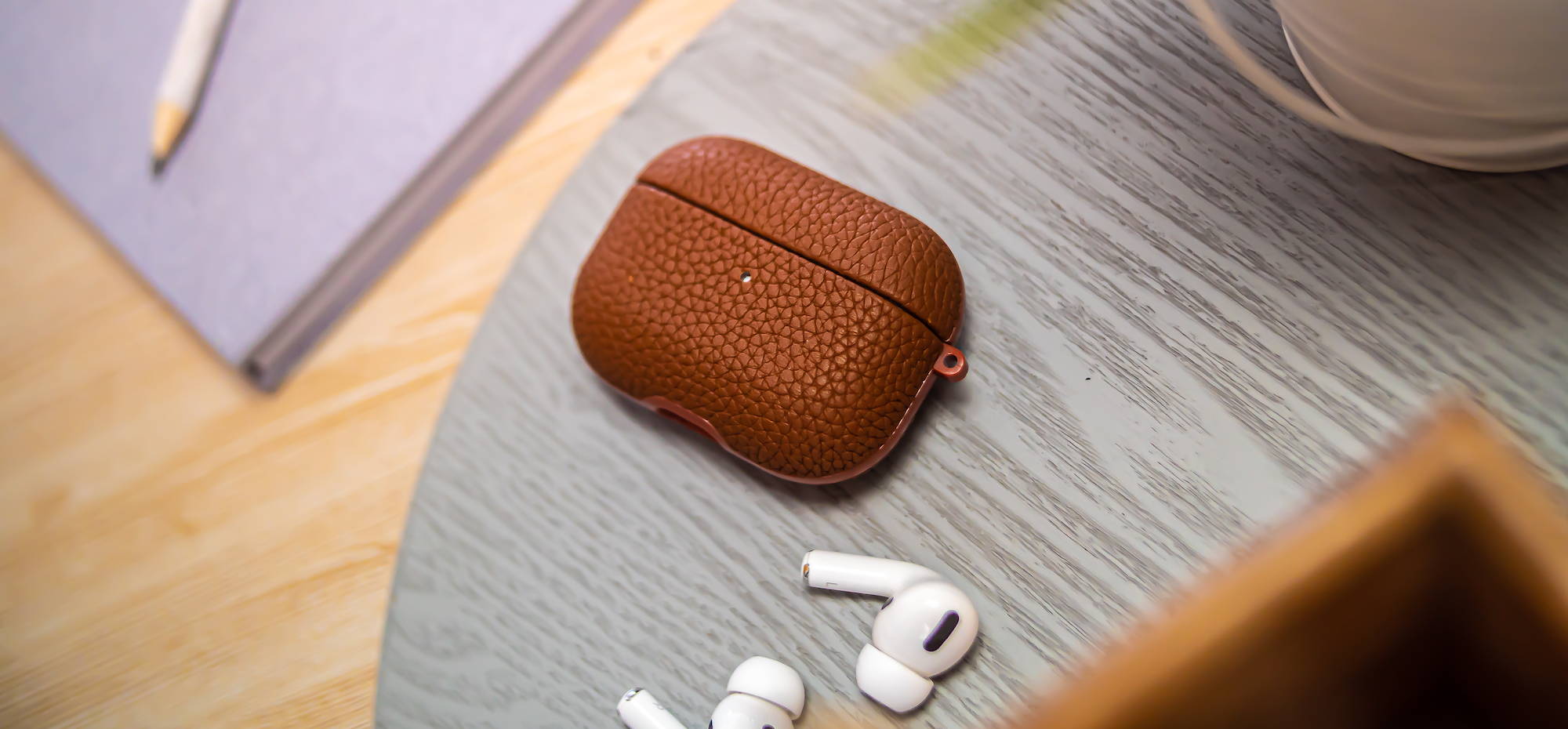 Brown genuine leather airpods pro case laying on grey wooden table 
