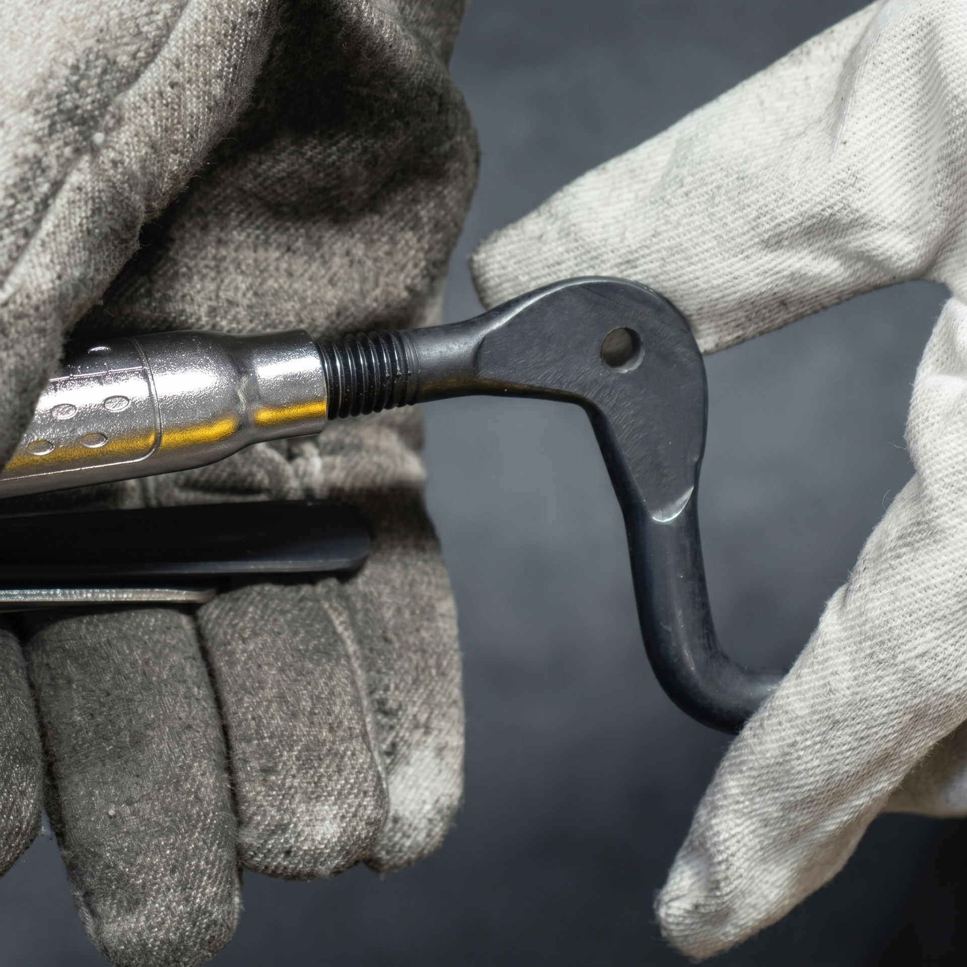 Gloved hands holding a metal hook tool against a dark background.