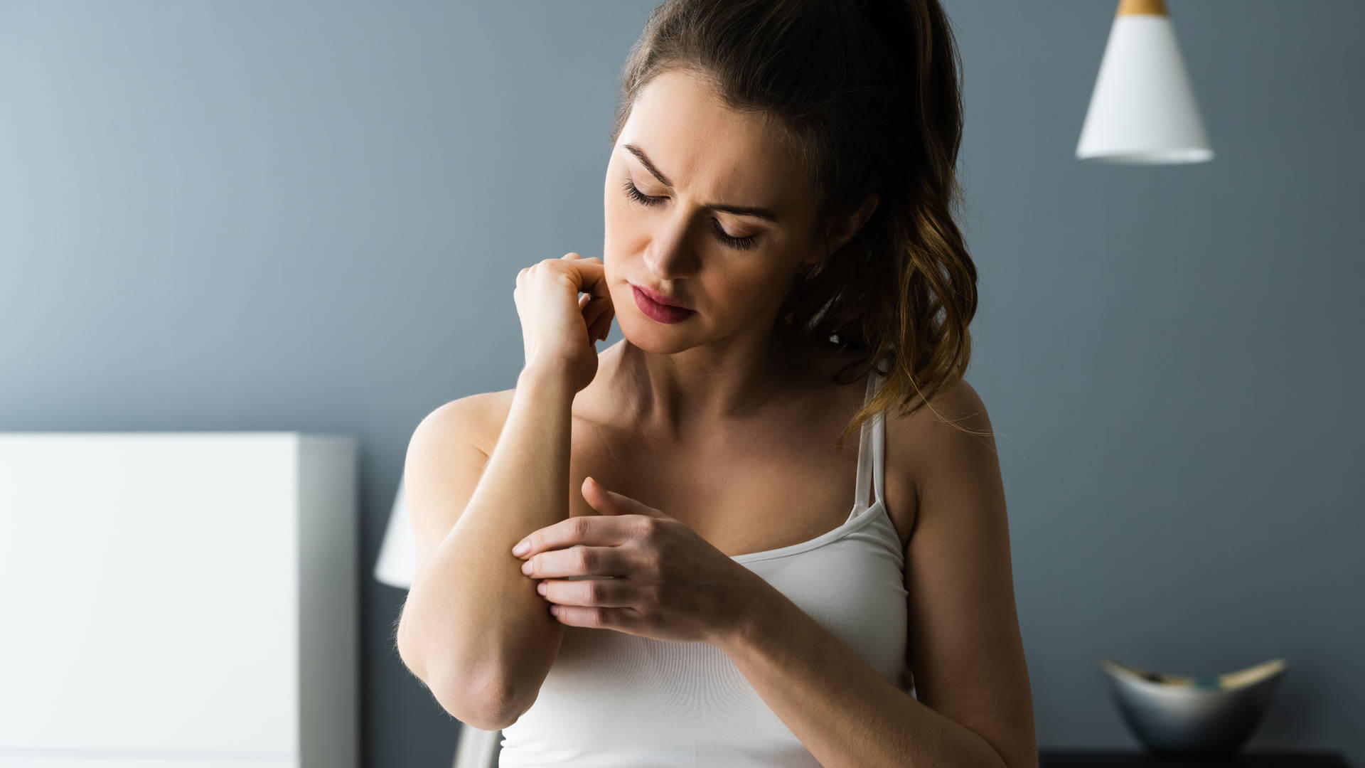 Junge Frau, die sich am Ellbogen kratzt. Die Symptome einer allergischen Kontaktdermatitis können innerhalb von Stunden oder über Wochen oder Monate auftreten.