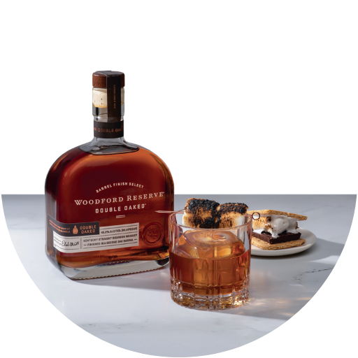 A bottle of Woodford Reserve with a glass and snacks.