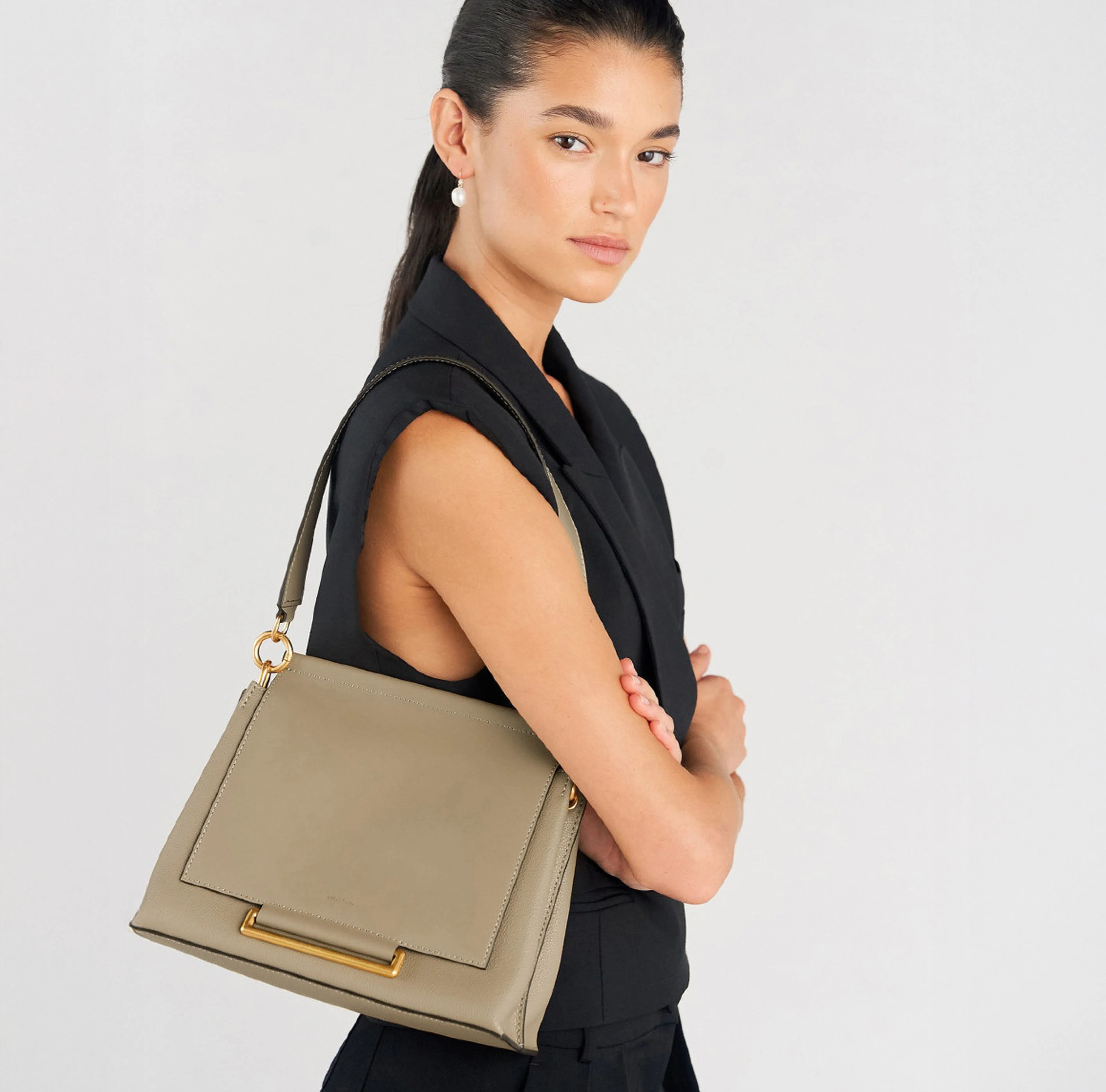A model wearing a black outfit, holding a beige handbag.