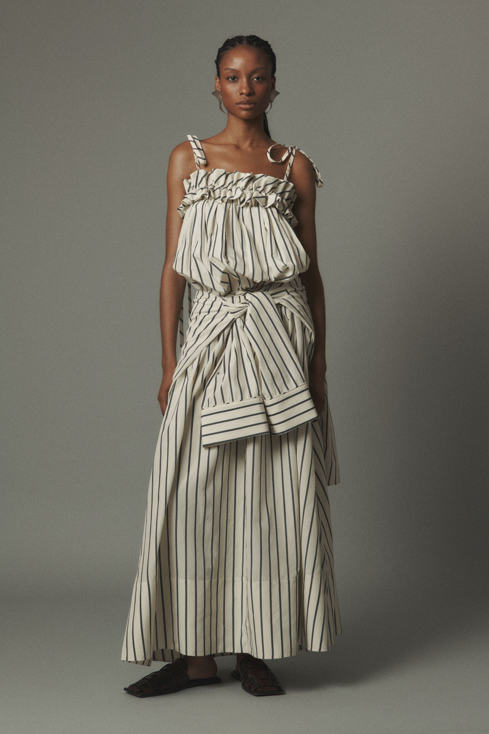 Model wearing a striped dress with a unique tie design and flat shoes.