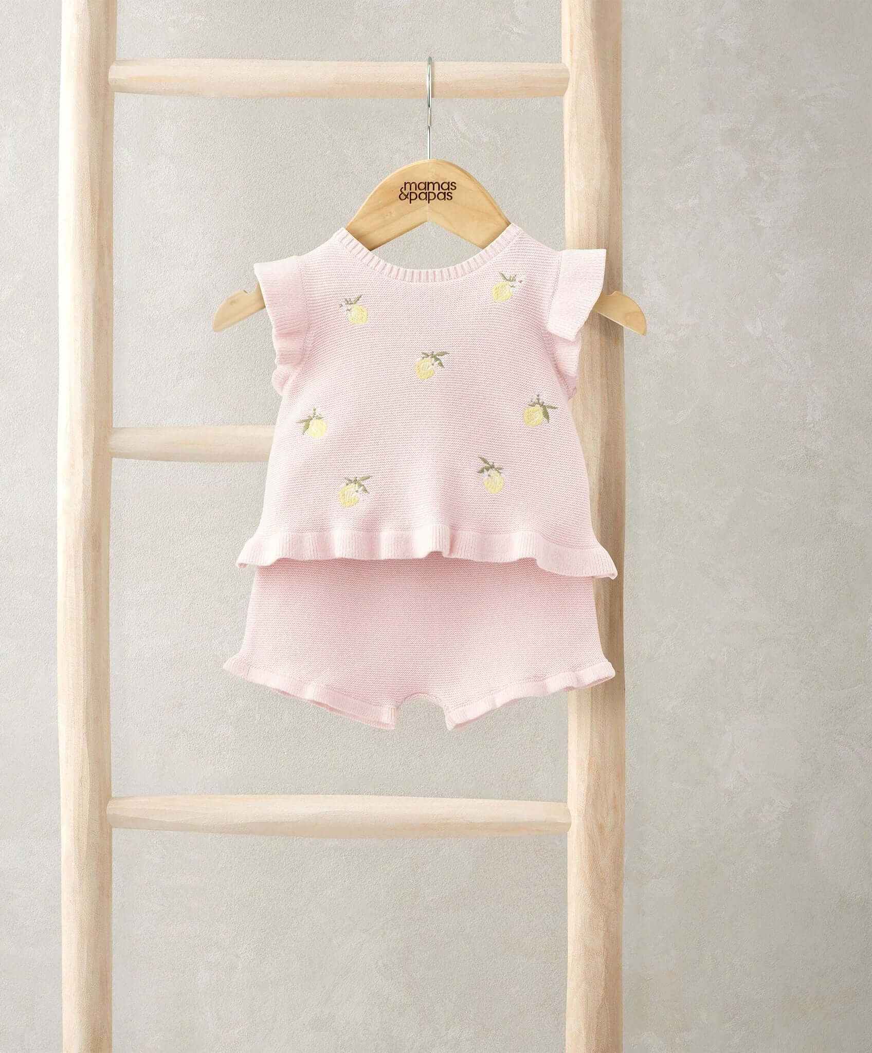 Pink children's outfit hanging on a wooden hanger against a neutral background.