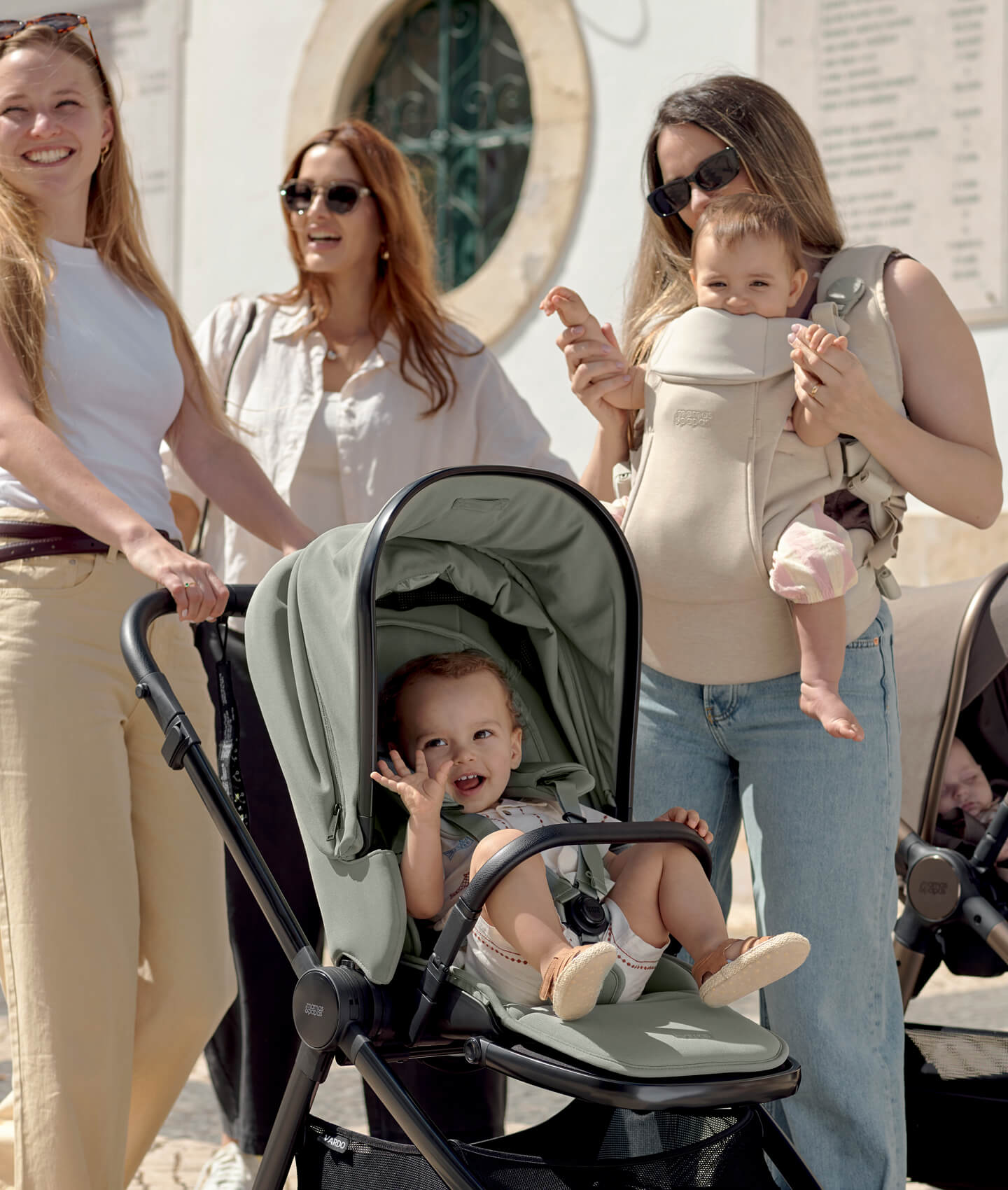 Four women with children, one in a stroller, outdoors.