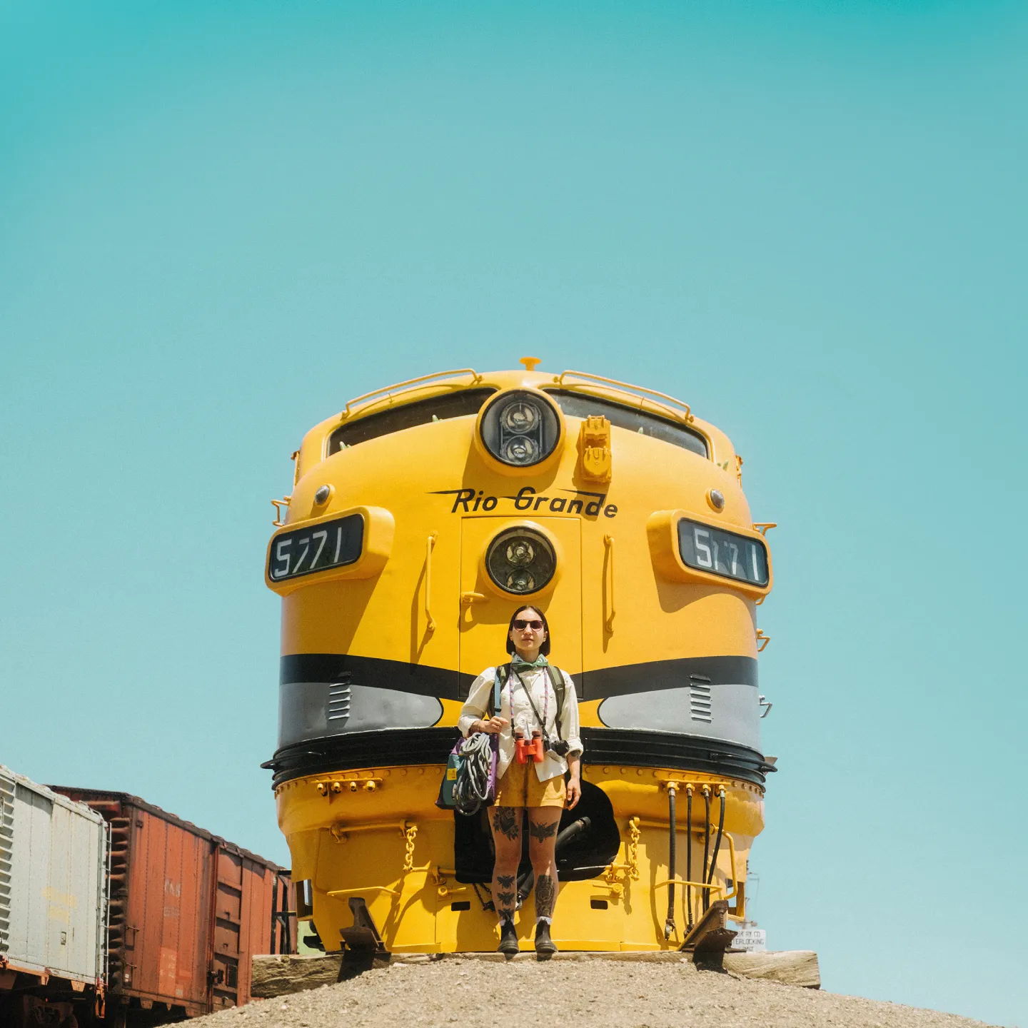Person standing in front of a large yellow train against a clear blue sky.