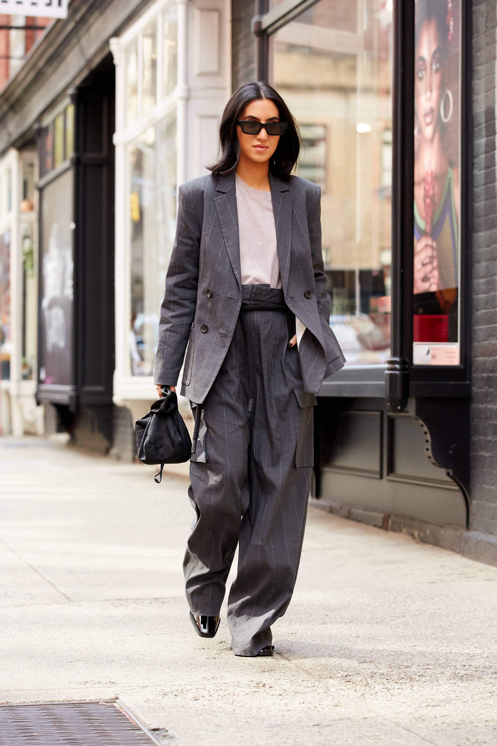 Person walking in stylish gray outfit with sunglasses on a city street.