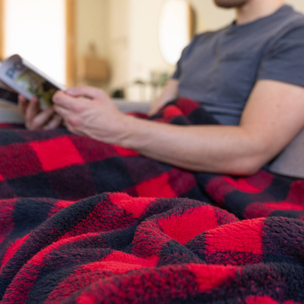 Man sitting on couch reading a magazine with Rumpl Sherpa Fleece blanket