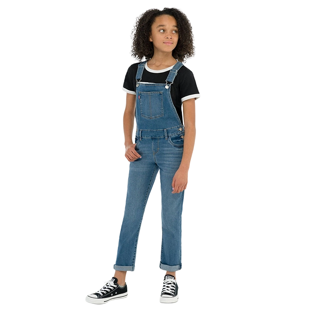 A girl wearing overalls and a black t-shirt with sneakers.