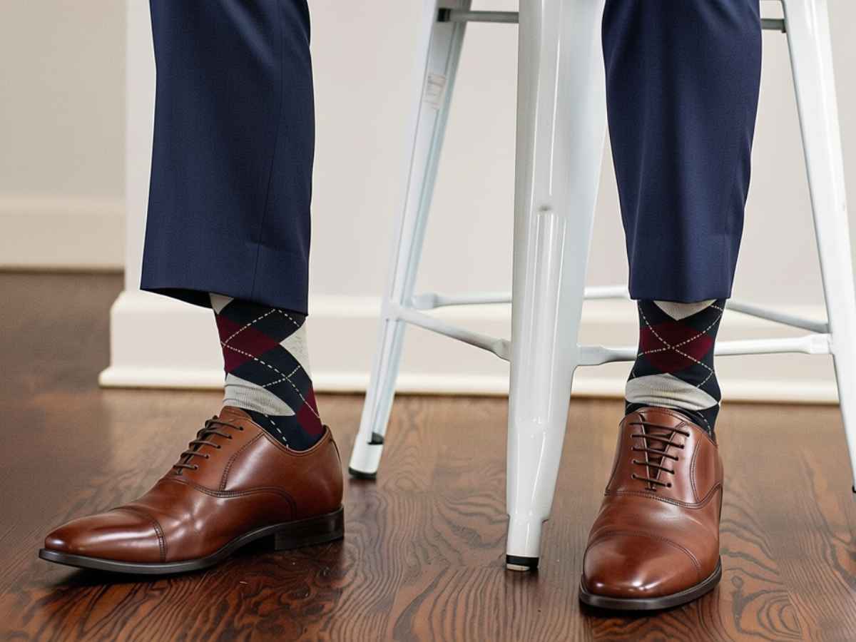 Man on stool wearing burgundy and navy argyle socks with navy dress pants and brown oxfords