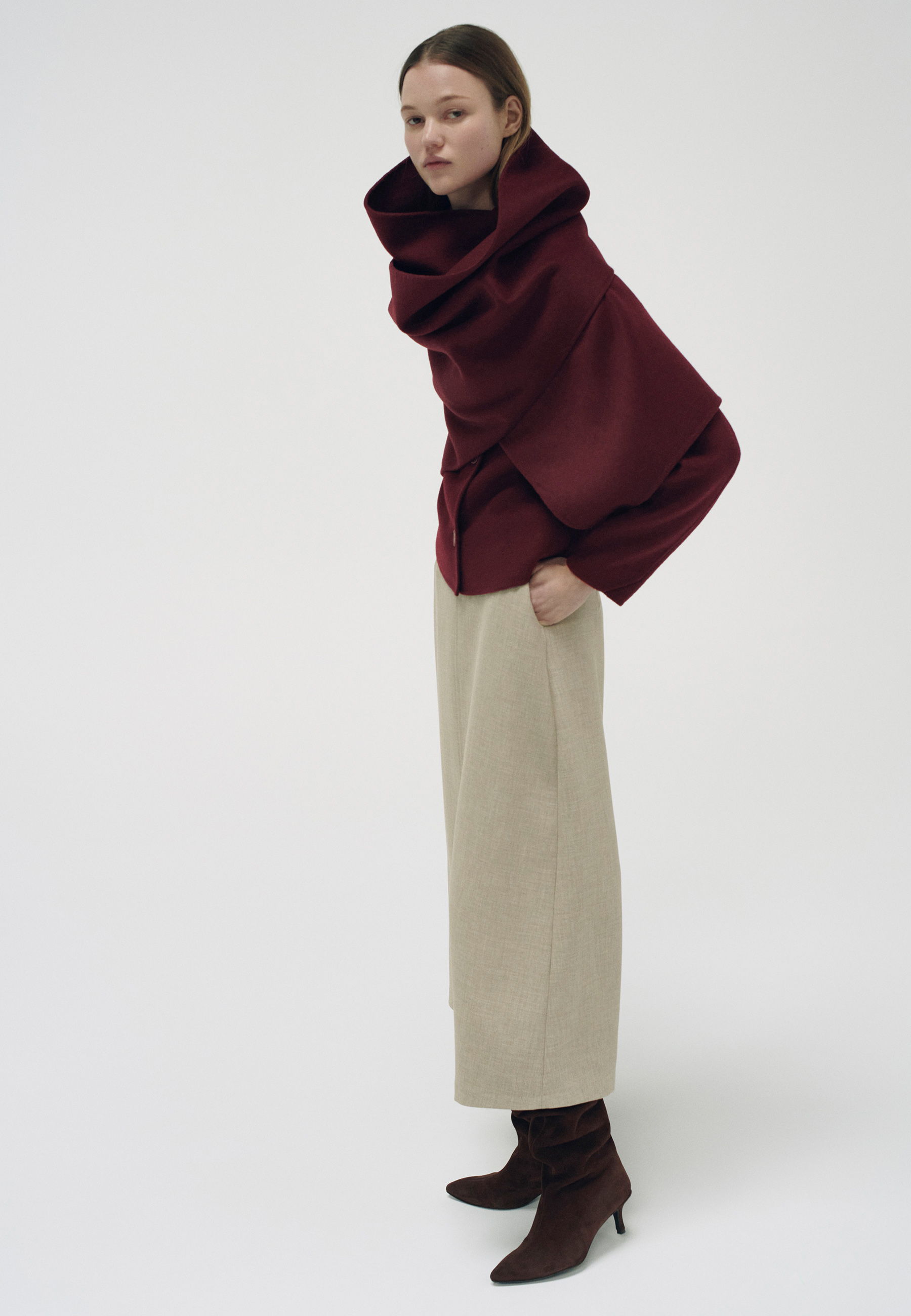 Model wearing a burgundy oversized top and beige wide-leg pants, standing sideways.
