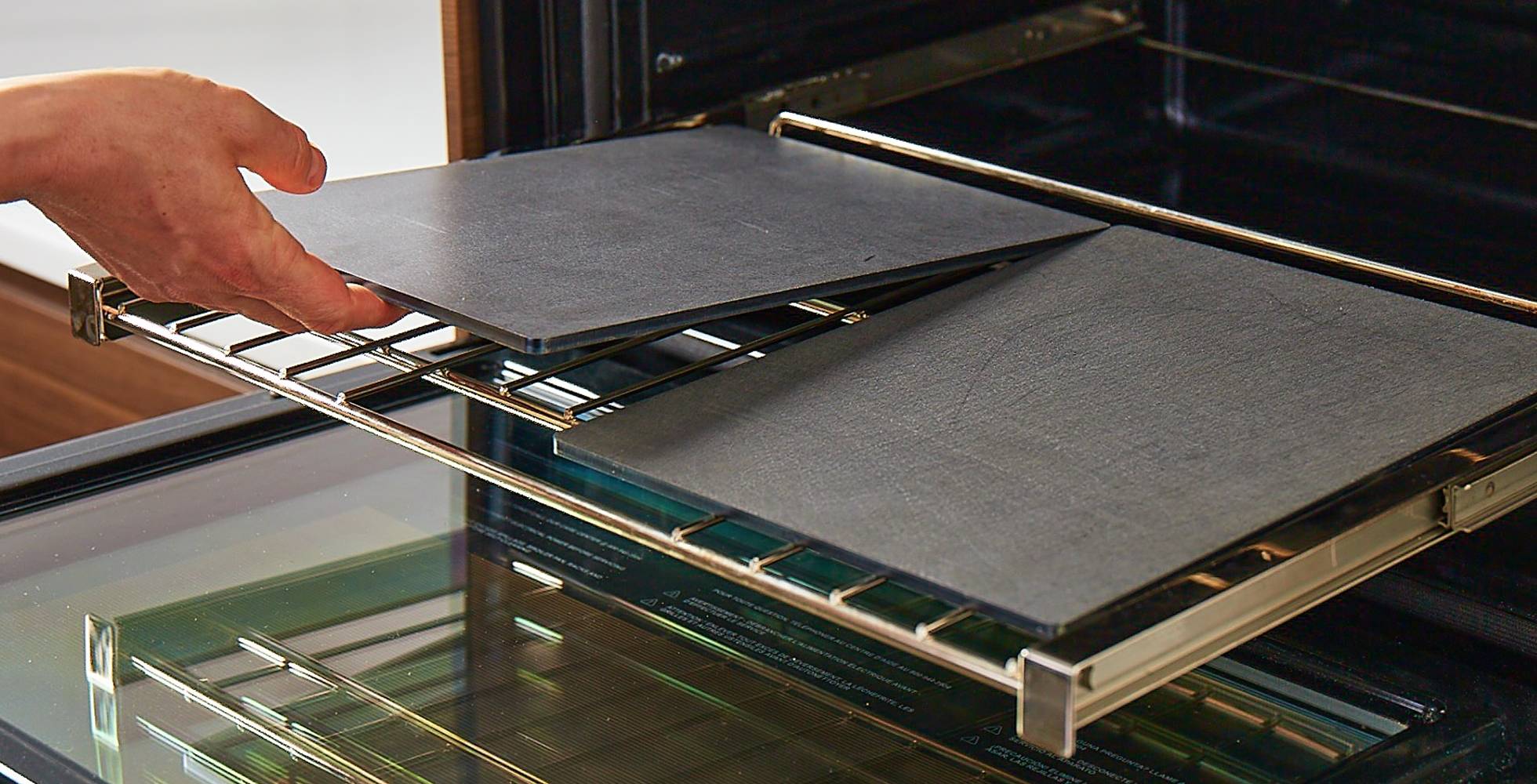 A hand places a Misen Oven Steel onto an oven rack next to another Misen Oven Steel, showing how they can fit neatly side-by-side.