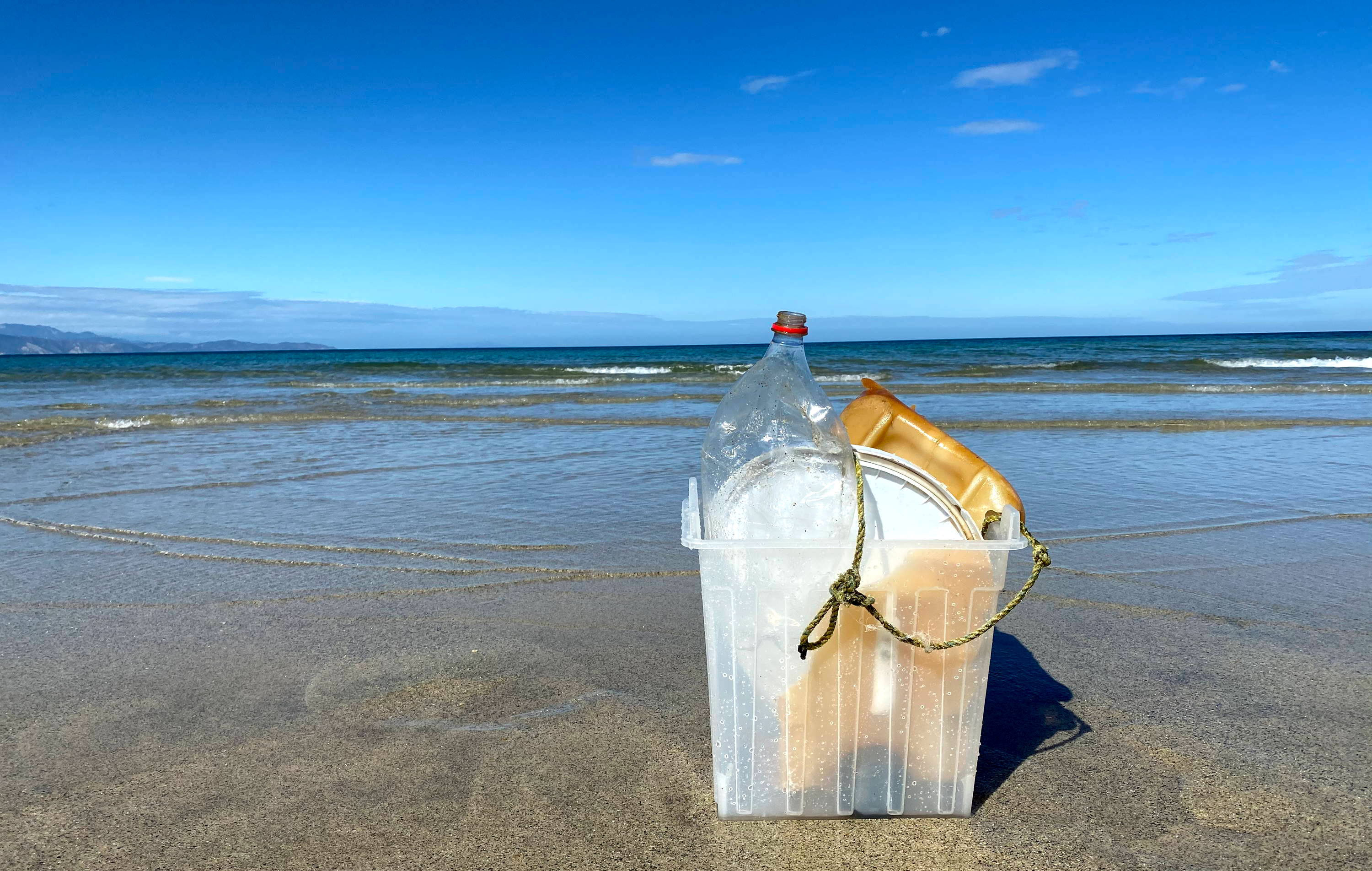 Garbage bin holding beach pollution beach with blue skies and clear water
