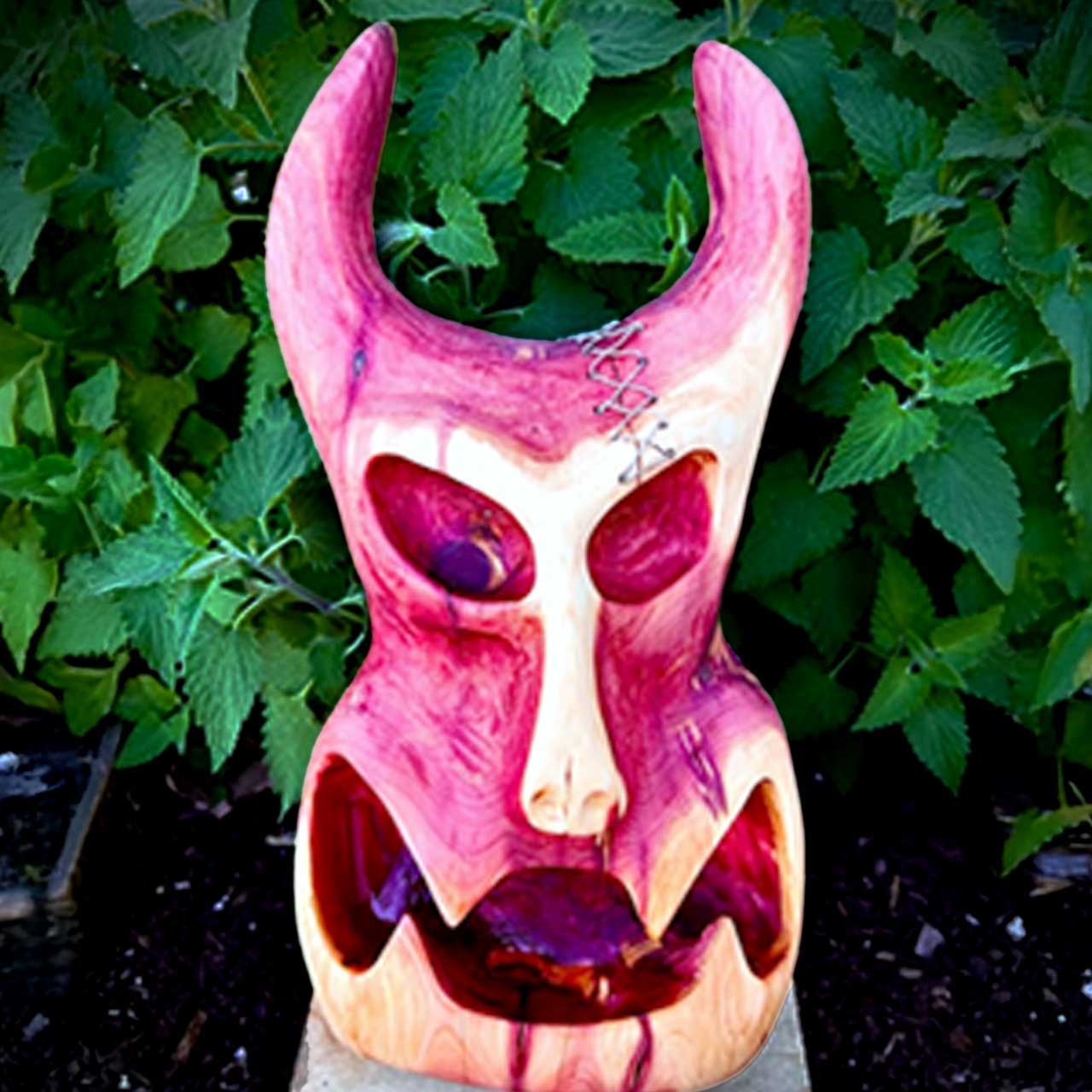 Colorful carved mask with horns against a backdrop of green leaves.
