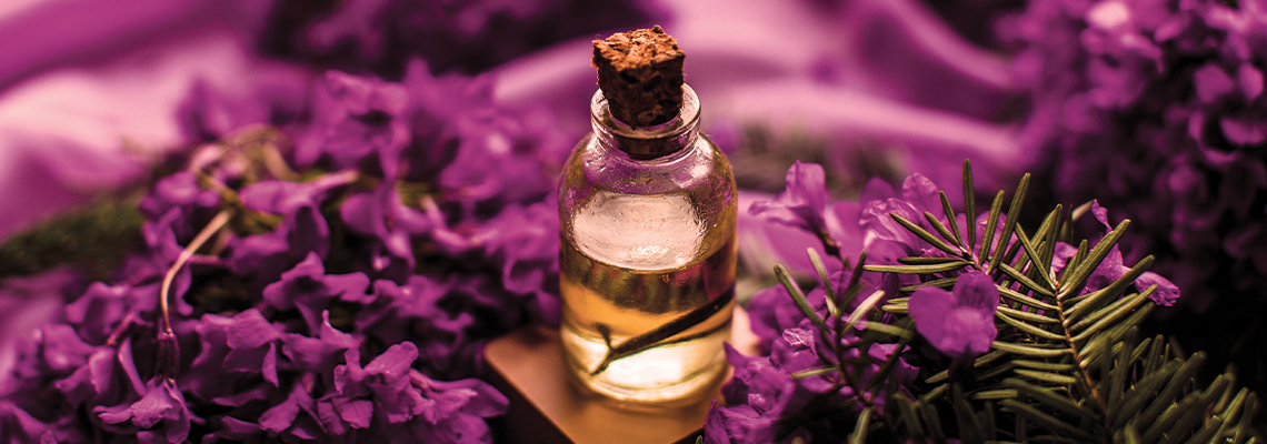 A small bottle of oil surrounded by purple flowers.