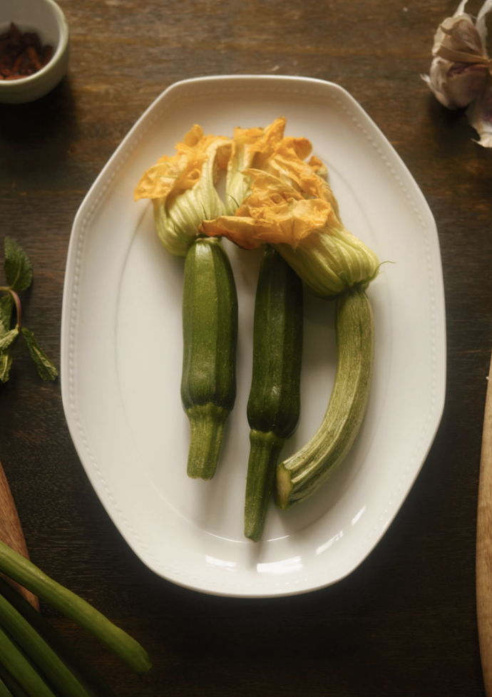 Fresh zucchini and squash blossoms on a white plate.