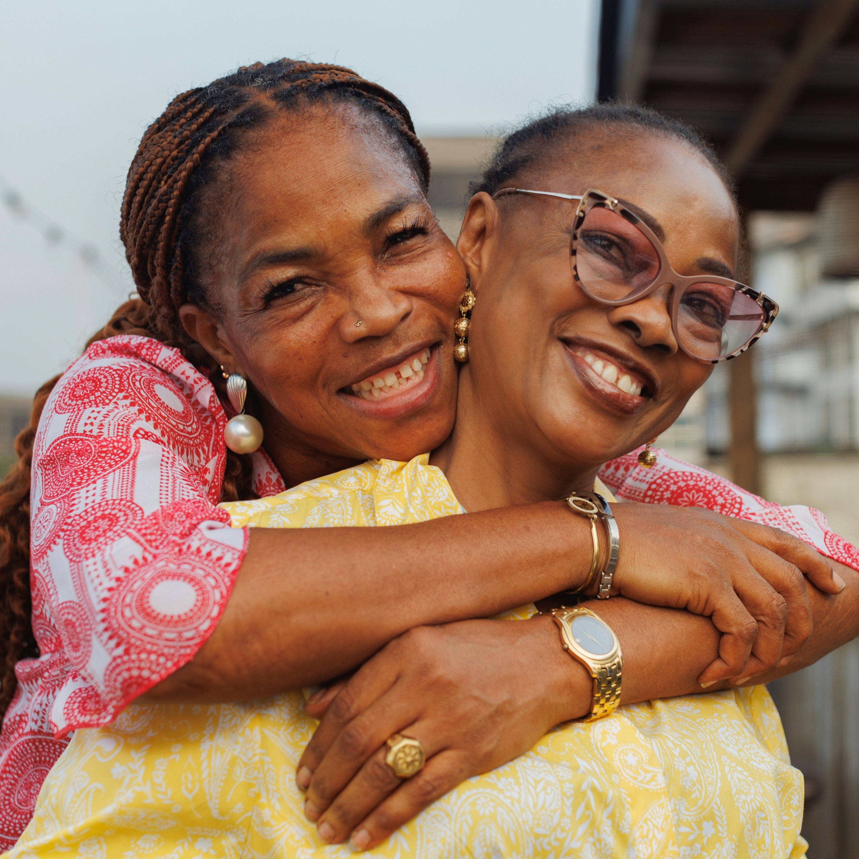 Two women smiling and embracing outdoors, enjoying a joyful moment together.