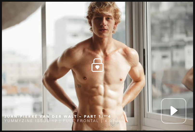 Muscular man standing indoors with hands on hips and a serious expression.